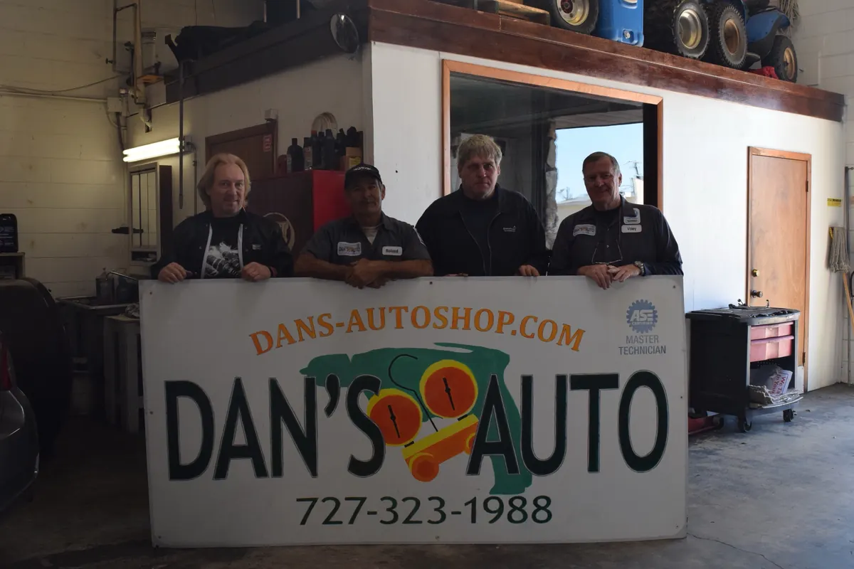 The Dan's Auto team standing behind the shop sign