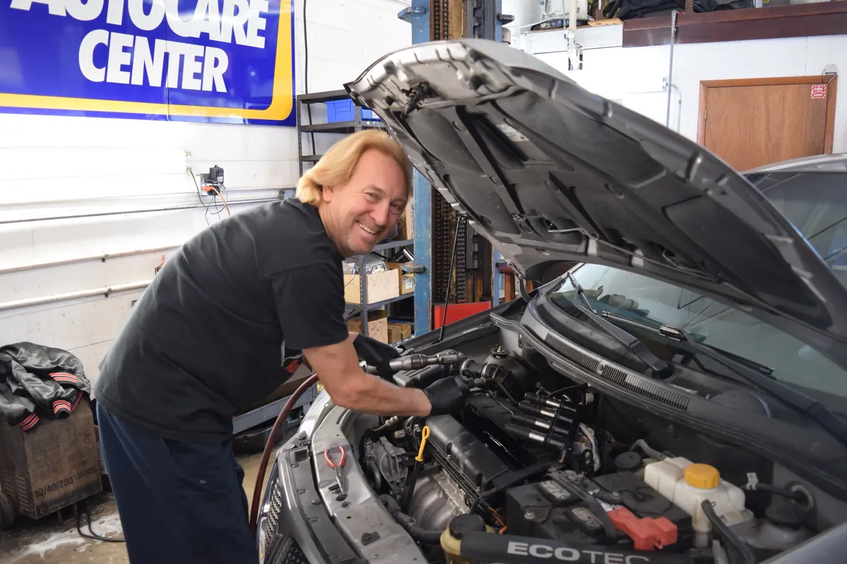 A member of the Dan's Auto team leaning over an open engine bay, smiling